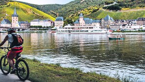 Un cycliste sur une piste cyclable au bord d’une rivière, avec un bateau et des bâtiments en arrière-plan.