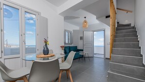 A modern interior with a dining area, a sofa, and a staircase. - Golden View Jacuzzi Suites (Santorini)