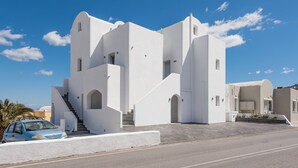 A white building with a staircase leading to a door, a car parked in front, and a clear blue sky. - Golden View Jacuzzi Suites (Santorini)