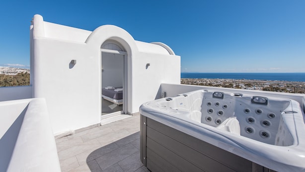A modern outdoor bathroom with a hot tub, a shower area, and a view of the coastline. - Golden View Jacuzzi Suites (Santorini)