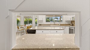 Una cocina moderna con armarios blancos, encimeras de granito y un comedor con sillas amarillas.