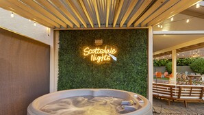 Zona de jacuzzi con un letrero de neón que dice "Scottsdale Nights" sobre un muro verde, rodeada de asientos al aire libre.