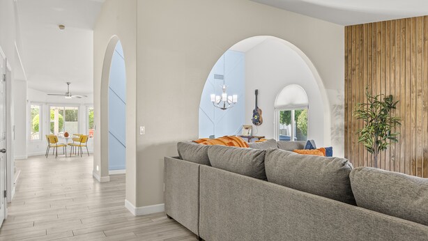 Una sala moderna con un sofá gris, panel de pared de madera y un comedor con sillas amarillas.