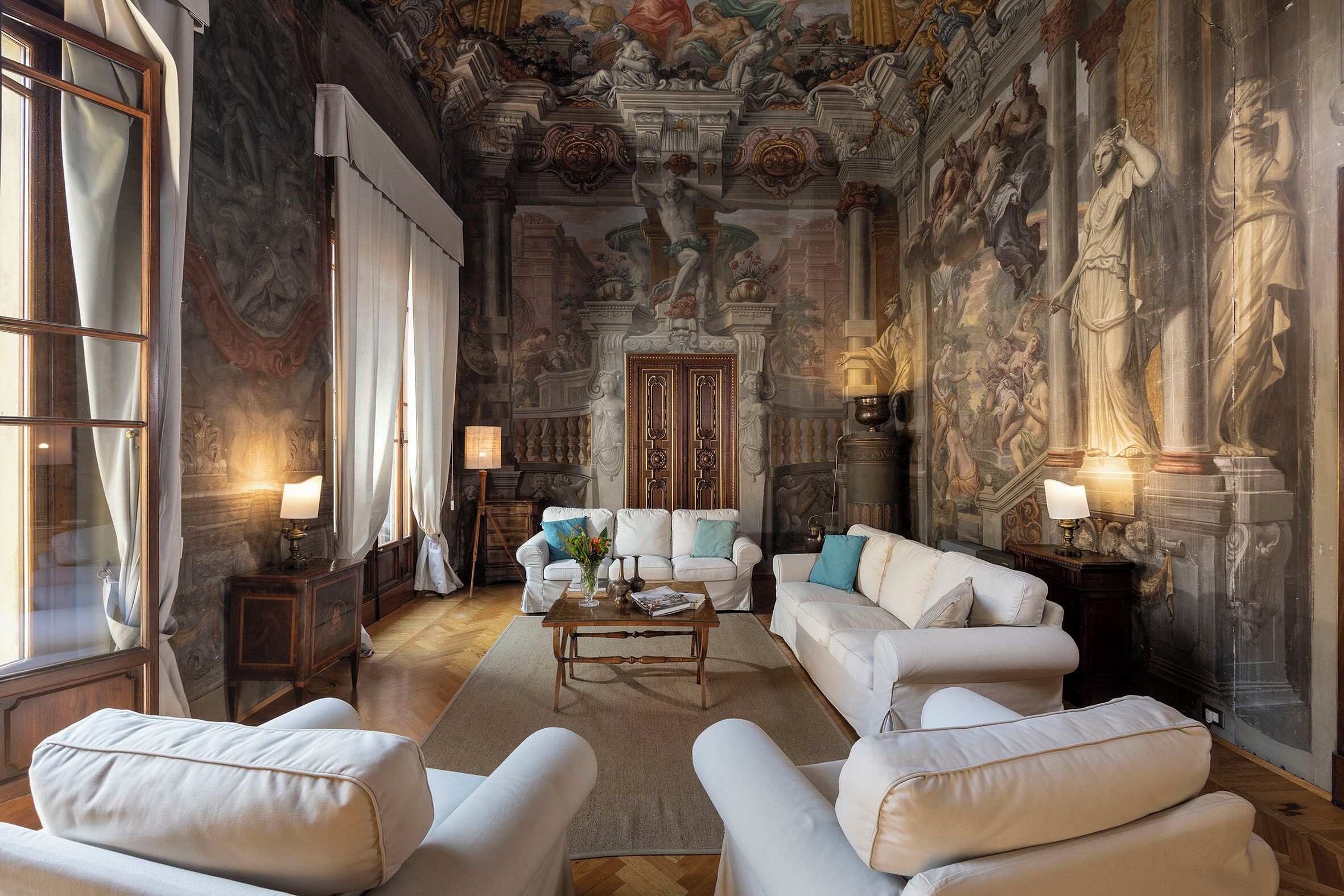 A luxurious room with classical frescoes, white furniture, and a grand entrance.
