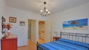 Une chambre à coucher comprenant un lit, une commode, un lustre, un tableau et une porte donnant sur une autre pièce.