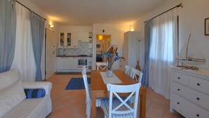 Un espace de vie compact comprenant un coin repas, une kitchenette et une maquette de voilier posée sur une commode.