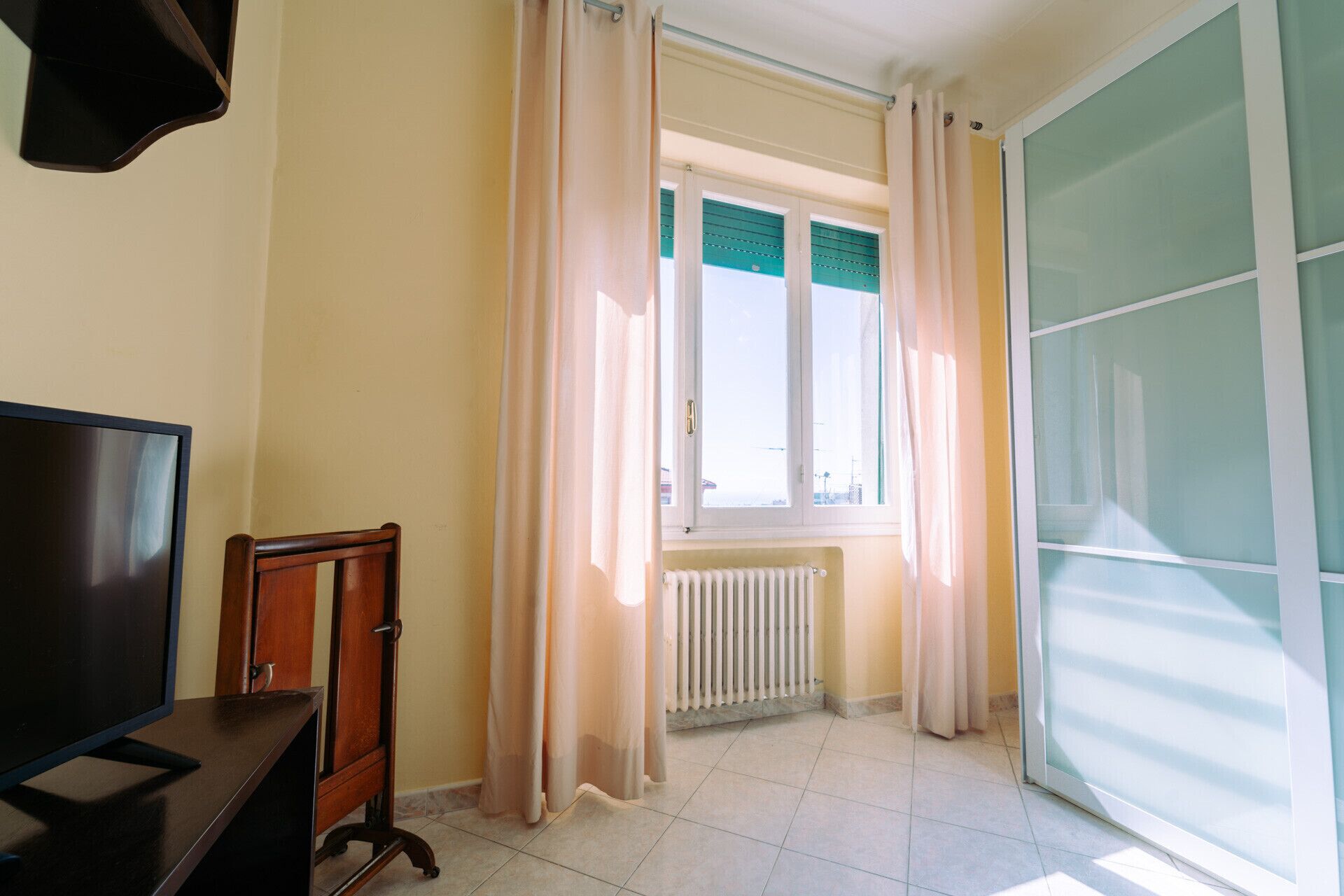 Une pièce dotée d’une grande fenêtre, d’un radiateur, d’un téléviseur et d’une porte coulissante.