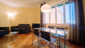 Ein modernes Wohnzimmer mit einem Glastisch, einer Ledersofa und einem großen Fenster mit Vorhängen.