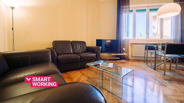Ein modernes Wohnzimmer mit einer Couch, einem Glastisch, einem Fernseher und einem Essbereich mit einem Stuhl und Tisch.