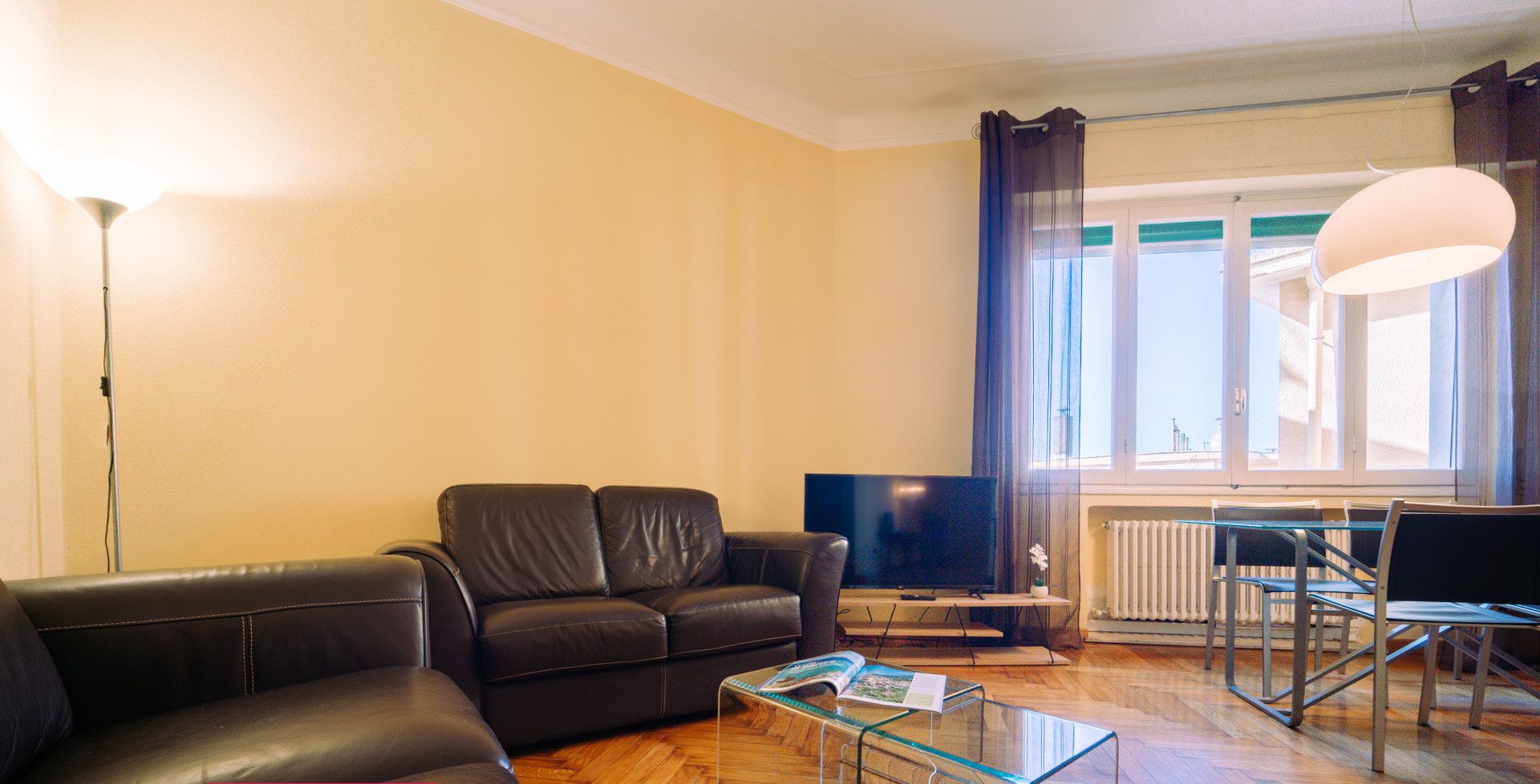 Un soggiorno moderno con un divano, un tavolino in vetro, una televisione e un’area pranzo con una sedia e un tavolo.