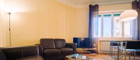 Un salon moderne comprenant un canapé, une table basse en verre, un téléviseur et un coin repas avec une chaise et une table.