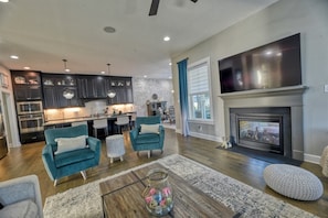 A modern living room with teal armchairs, a fireplace, and a kitchen in the background.