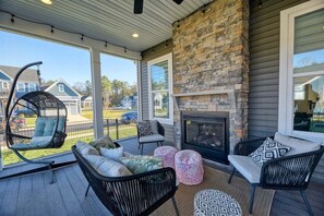 A covered outdoor seating area with a fireplace, wicker chairs, and ottomans. - Coastal Club * 18353 * NEW Exceptional Lewes Beach House (Lewes)