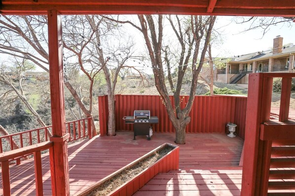 A covered outdoor deck with a barbecue grill, surrounded by red railings and a tree. - Luxurious Spanish Renaissance in Ransom Canyon 4/3 (Lubbock)
