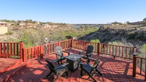 Une terrasse en bois avec une rambarde rouge, des meubles d’extérieur et une vue panoramique sur une vallée parsemée de maisons et bordée d’un plan d’eau.