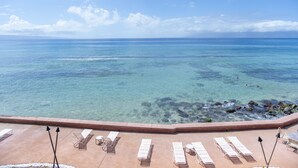A poolside view with clear blue water, lounge chairs, and a view of the ocean. - New Unit To rental Program (Lahaina)