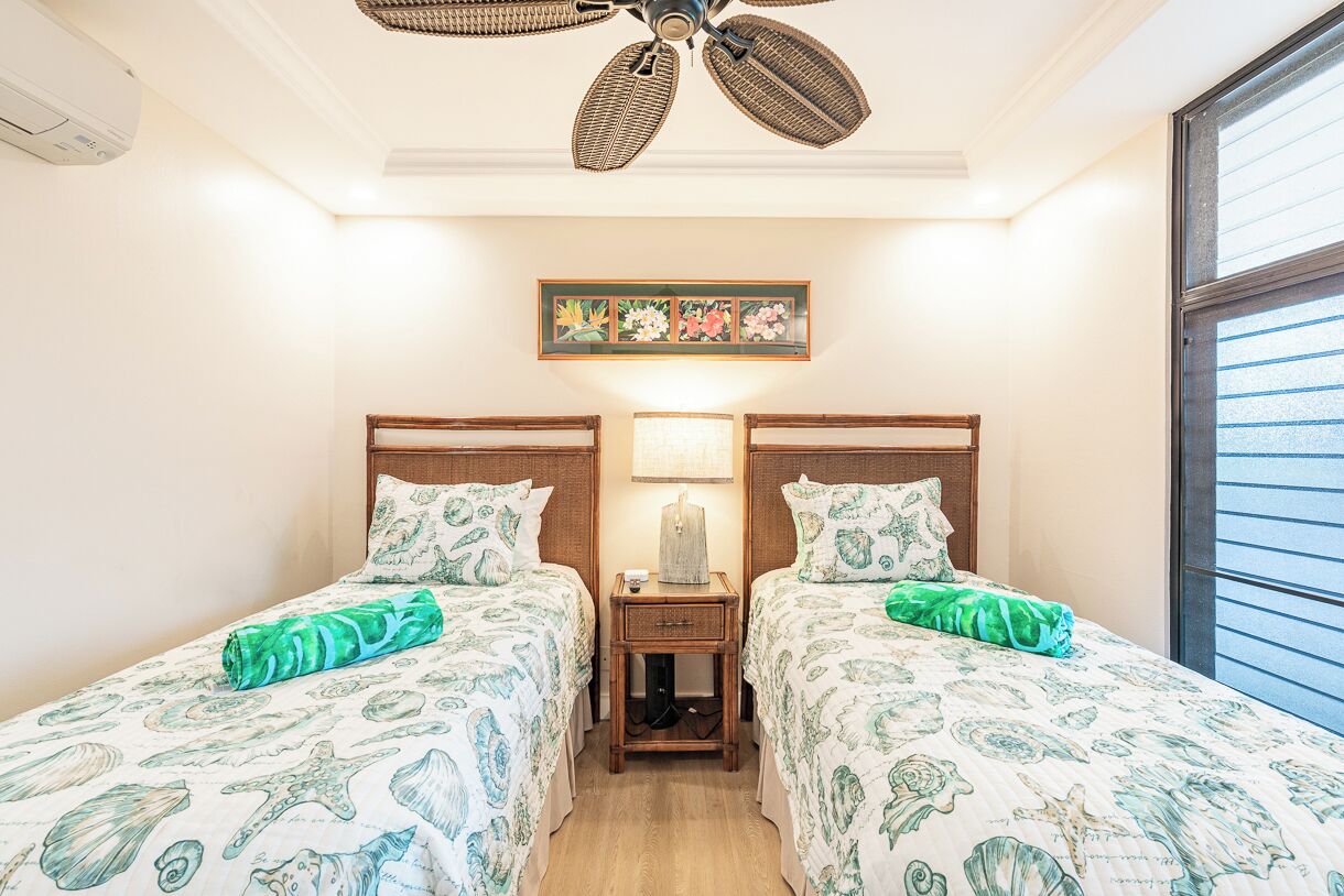Une chambre d’hôtel avec deux lits, un ventilateur de plafond, une table de chevet, une lampe et une fenêtre.
