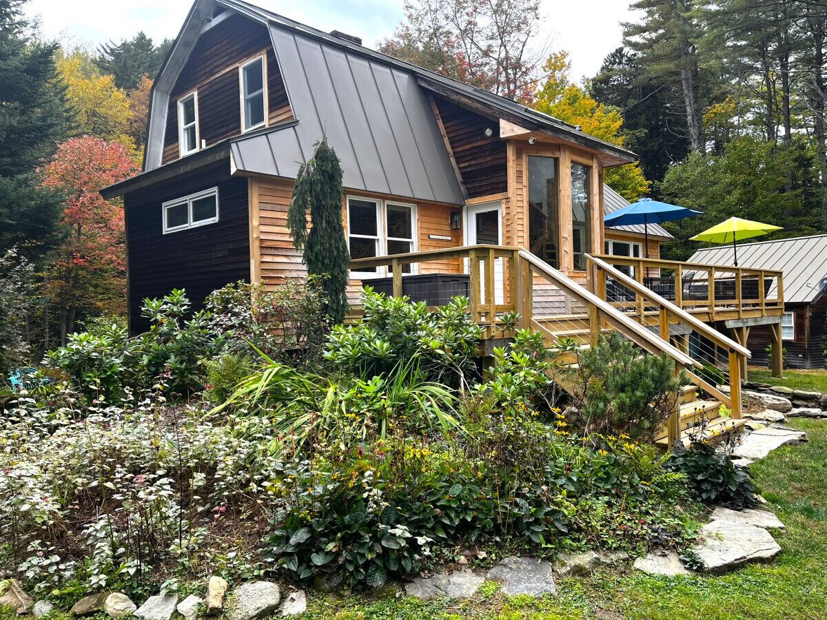 A two-story log cabin with a wooden deck and a staircase leading to the upper floor.