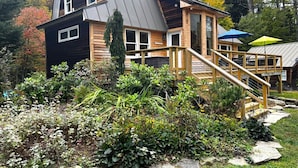 A two-story log cabin with a wooden deck and a staircase leading to the upper floor. - Chalet- Stream, A/C, Hot Tub, min to Lake and Ski (Whitingham)