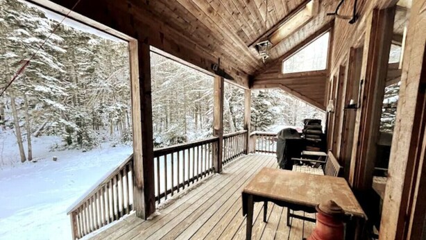 A wooden deck with a table and chairs, overlooking a snowy forest. - Chalet- Stream, A/C, Hot Tub, min to Lake and Ski (Whitingham)