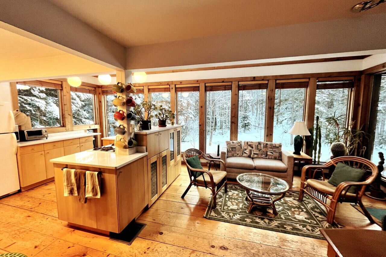 Un intérieur chaleureux comprenant une cuisine, un coin repas et un espace salon avec de grandes fenêtres.