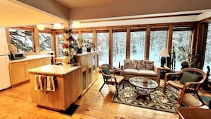 A cozy interior with a kitchen, dining area, and seating space with large windows. - Chalet- Stream, A/C, Hot Tub, min to Lake and Ski (Whitingham)