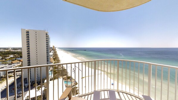 Uma varanda com vista para uma praia, um cais e um edifício alto.