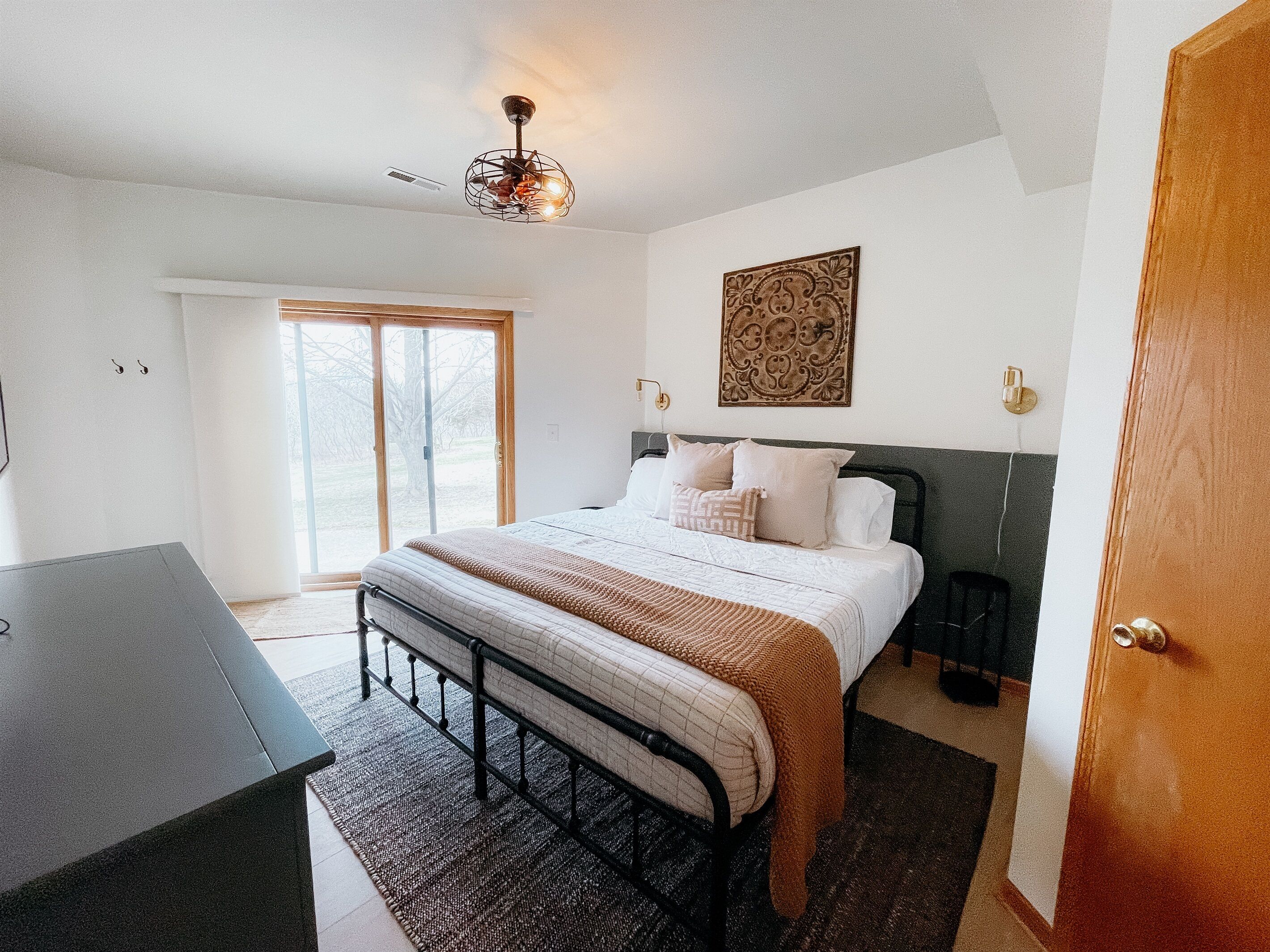Une chambre à coucher avec un lit, des tables de chevet, un bureau, une fenêtre et une porte.