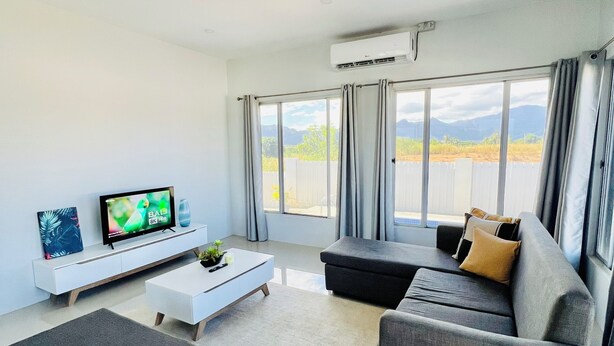 Una sala de estar moderna con una televisión de pantalla plana, una consola blanca, un sofá gris y un amplio ventanal con cortinas.