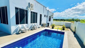 Una casa moderna con piscina, ventanas amplias y mobiliario exterior.