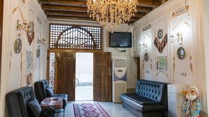 A room with a chandelier, two sofas, a television, and decorative wall art. - Grand Nodirbek Boutique Hotel - House Museum 17-19 century (Bukhara)