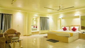 A hotel room with a bed, a chair, a table, and a ceiling fan. - Hotel Saptarshi (Bankura)