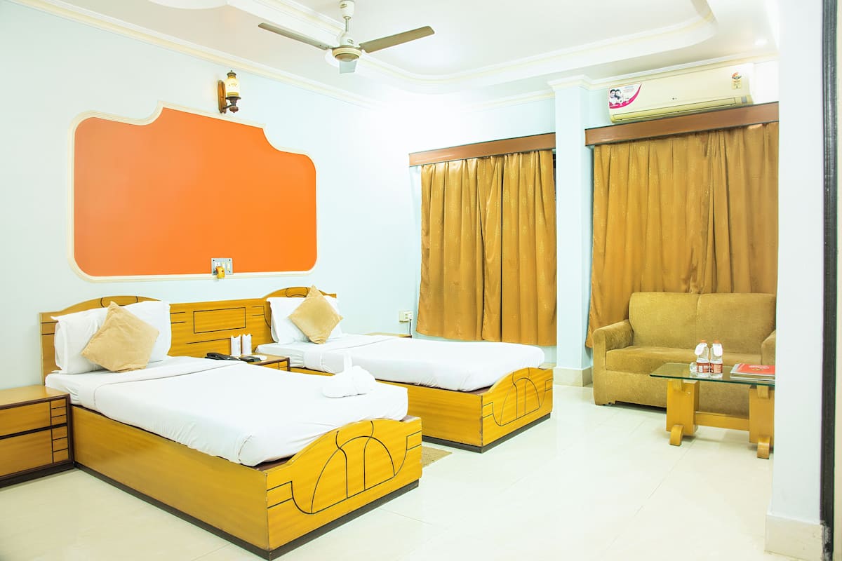 A hotel room with two beds, a sofa, a small table, and a ceiling fan.