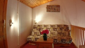 A cozy room with a wooden ceiling, a patterned sofa, a small table with a vase of flowers, and a wall-mounted light fixture. - 100m from ski slopes, 4th floor, view mountain, tv, ski locker, 61m², Valmorel (Valmorel)