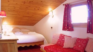 A cozy room with a wooden ceiling, a bed with white linens, a red sofa with patterned cushions, and a window with star-patterned curtains. - 100m from ski slopes, 4th floor, view mountain, tv, ski locker, 61m², Valmorel (Valmorel)