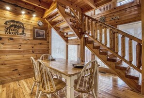 A wooden interior with a dining area, a staircase, and a wall-mounted clock.