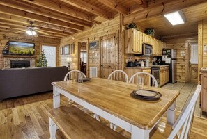 Interior de una cabaña de madera con comedor, cocina y chimenea.