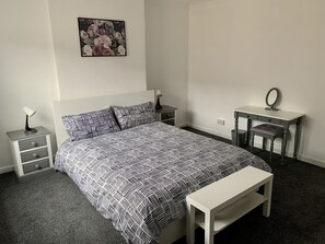 Ein Schlafzimmer mit Bett, Nachttischen, einem Schreibtisch, einer Bank und einem wandmontierten Spiegel.