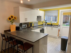 Eine moderne Küche mit weißen Schränken, einer zentralen Kochinsel mit Barhocker, einer Mikrowelle, einem Toaster und einer Tafel mit Anweisungen.
