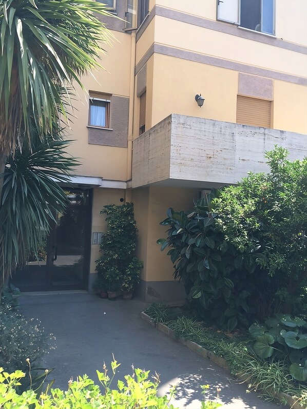 Ein Gebäude mit einer gelben Fassade, einer schwarzen Tür und Blumentöpfen vor dem Eingang.
