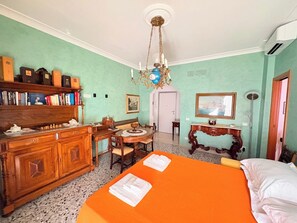 Una stanza con un letto, una scrivania, una sedia, una libreria, un lampadario e un quadro appeso al muro.