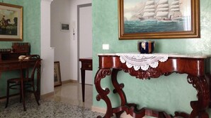 Una habitación con una pared verde, un cuadro enmarcado de un barco a vela, una mesa de madera con mantel de encaje y un escritorio con una silla.