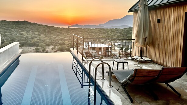Une piscine à débordement offrant une vue sur un coucher de soleil se reflétant sur un paysage montagneux.