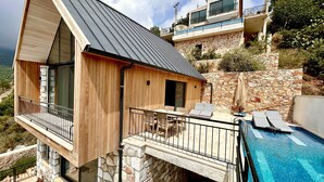 Une villa moderne avec une façade en pierre, un balcon doté d’un espace salon et un espace piscine.