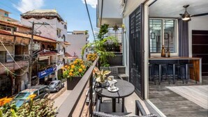 Un balcone cittadino stretto con un tavolino e sedie, piante in vaso e vista sugli edifici limitrofi.