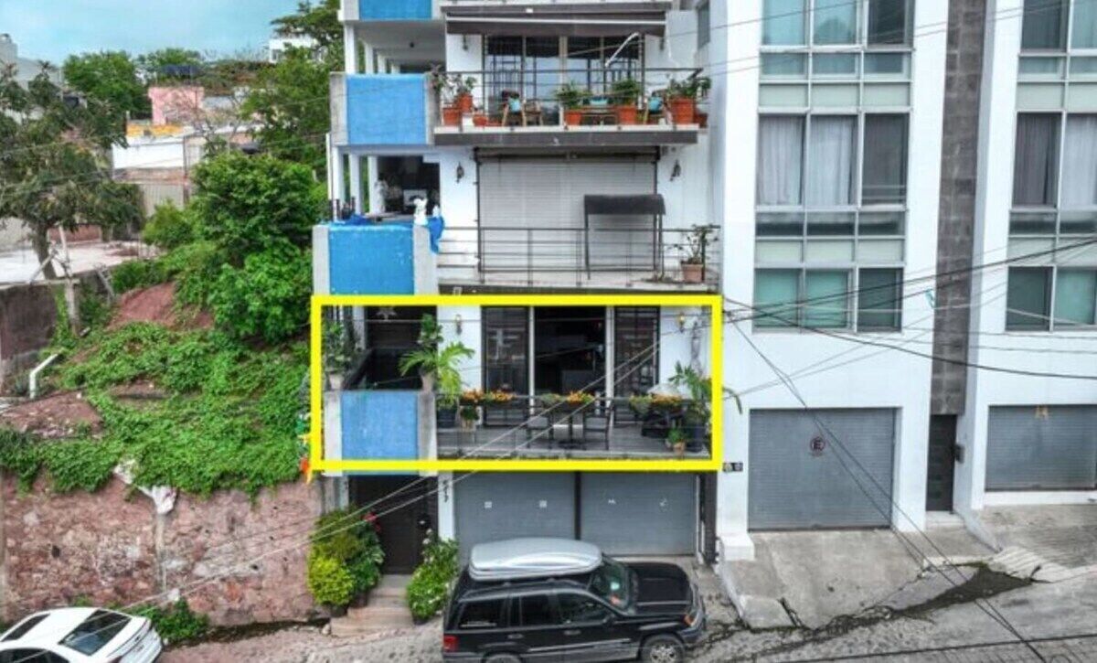 Un edificio de varios pisos con un balcón en el segundo piso, un garaje en la planta baja, y un coche estacionado al frente.