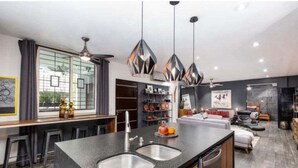 Una cucina moderna con isola centrale, sgabelli da bar, illuminazione a sospensione e vista sull'area soggiorno.