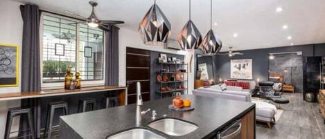 A modern kitchen with a central island, bar stools, pendant lighting, and a view of the living area.