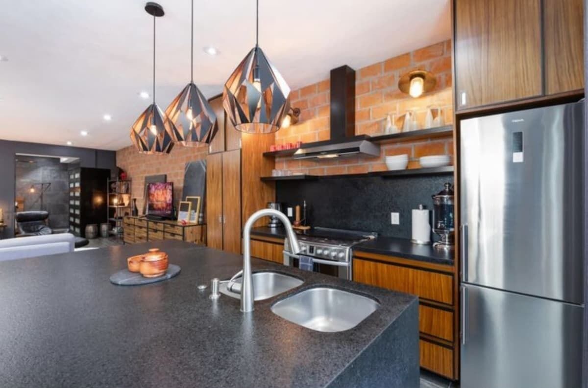 A modern kitchen with a central island, stainless steel appliances, and a brick accent wall.