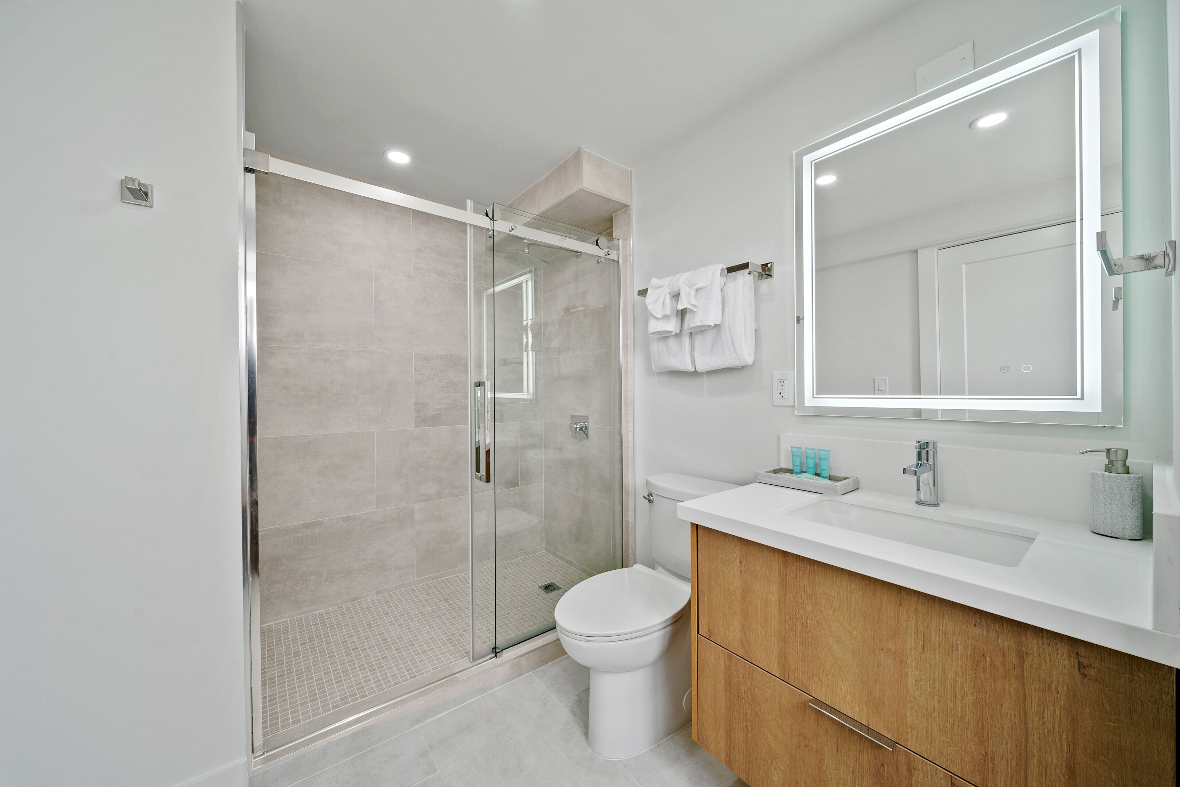 A modern bathroom with a glass-enclosed shower, a white toilet, and a wooden vanity with a mirror.